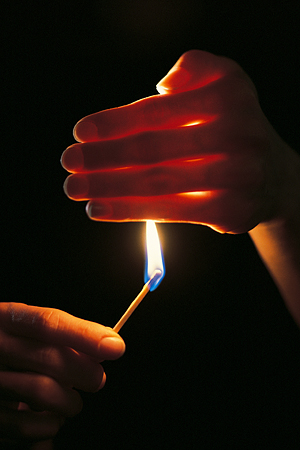 A lit match being shielded by a human hand