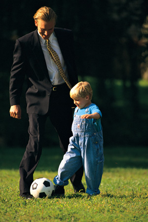 Father and son kicking soccer ball on lawn