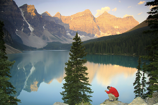 Majestic mountains reflected in lake, with single man kneeling in prayer in forefront